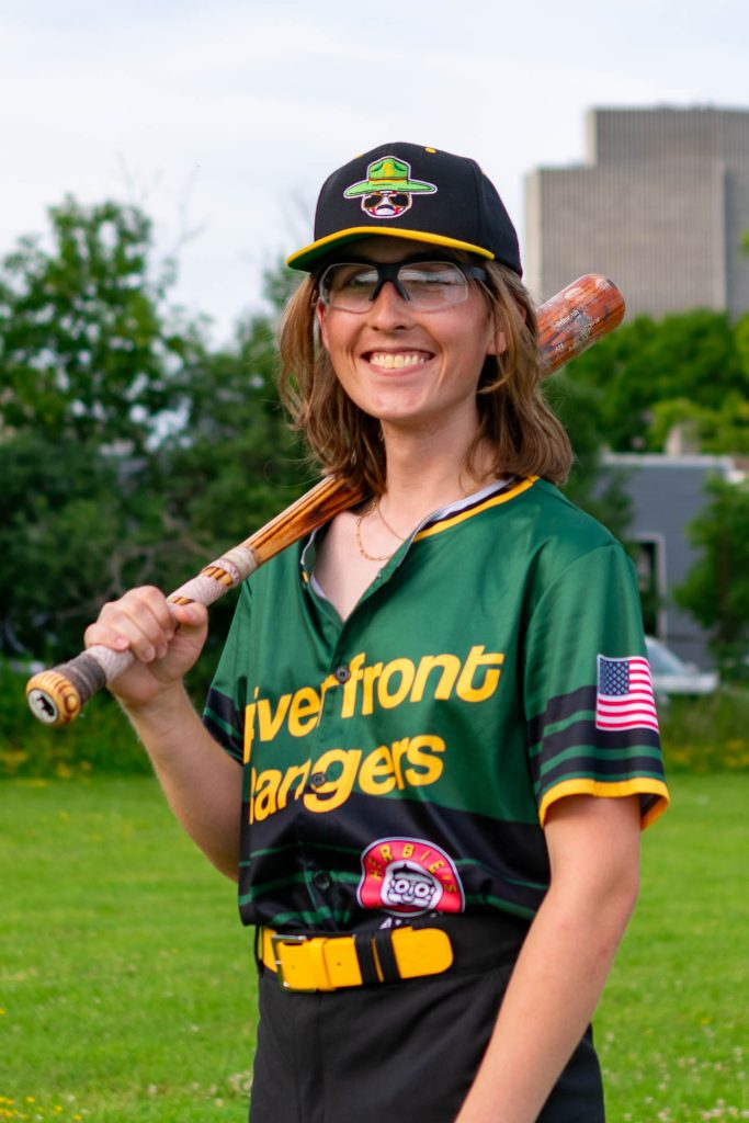 Rand posing with a bat at "Ant Field" in Albany, NY with the Corning Tower in the background.